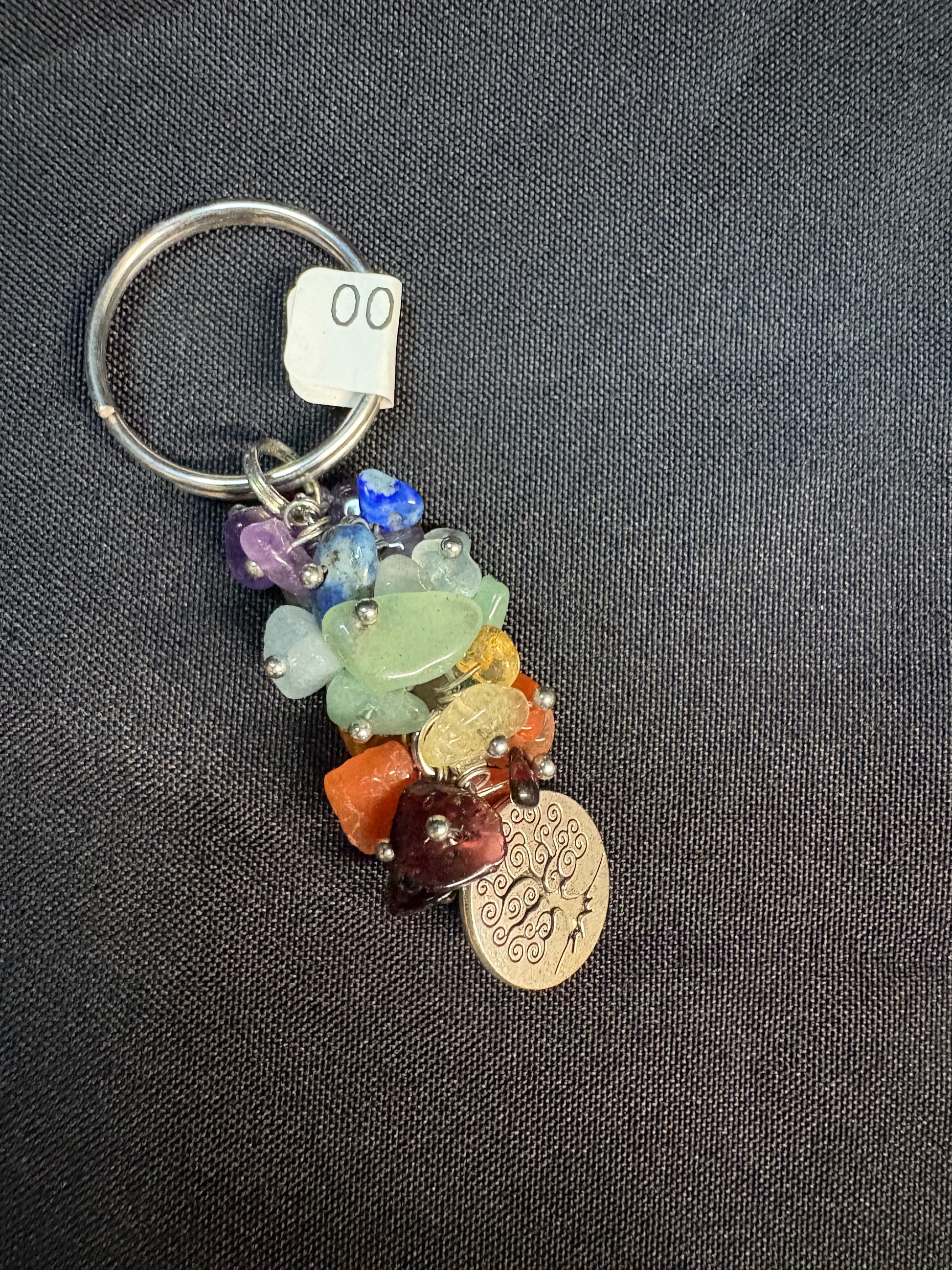 Keychain with colorful beads and a coin charm on a dark fabric background Chakra Stones
