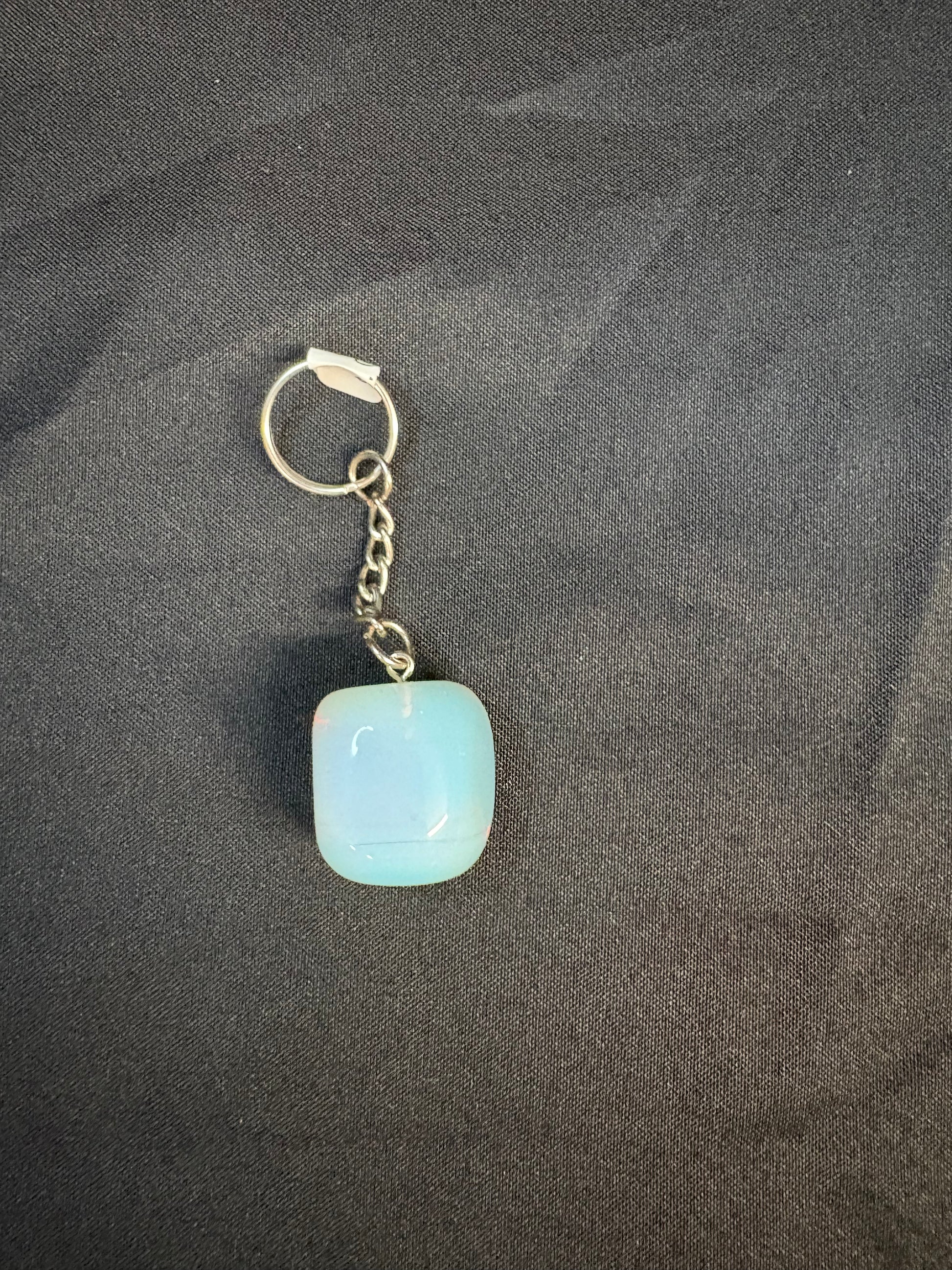 Keychain with a light blue square pendant on a dark fabric background opalite