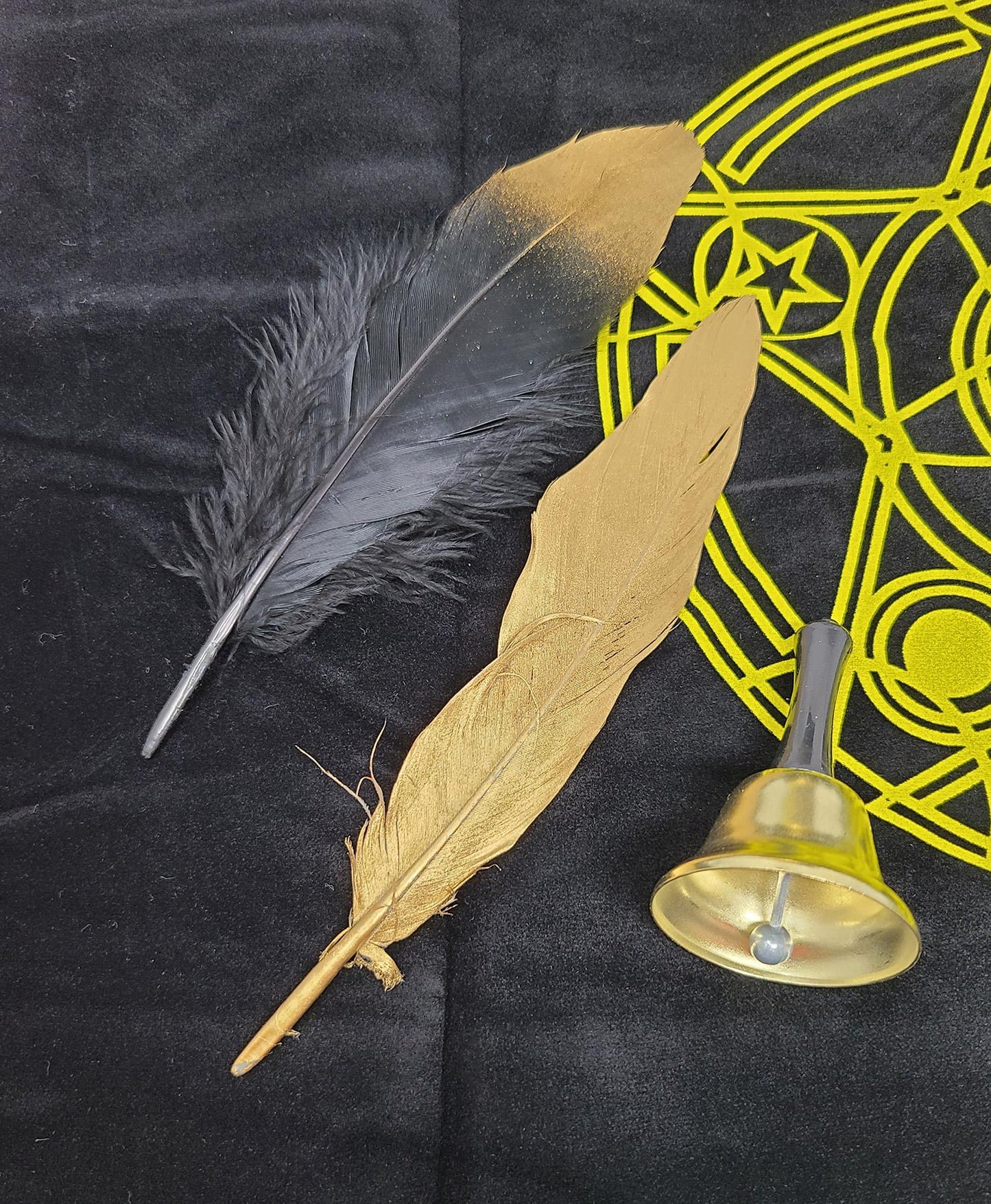 Two feathers and a small bell on a black background with yellow geometric design